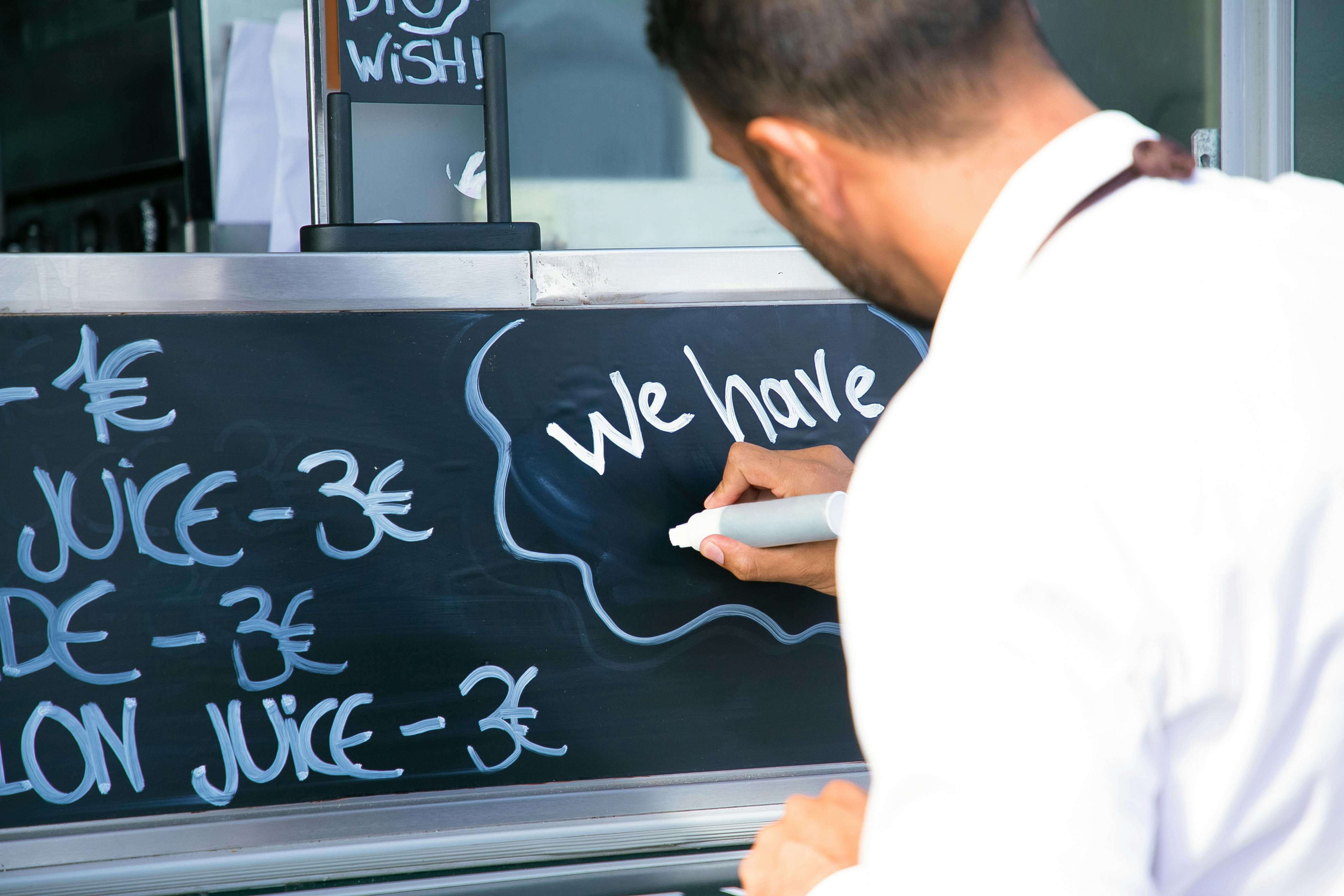 man writing menu on board on food truck