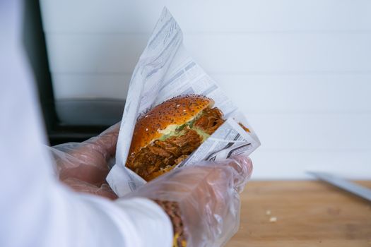 Crop anonymous male seller preparing order of burger with fried pork and bun with sesame