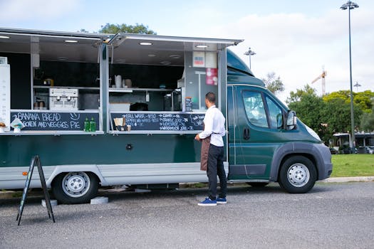 Back view full body of anonymous man in apron standing near food trailer with counter and menu on board