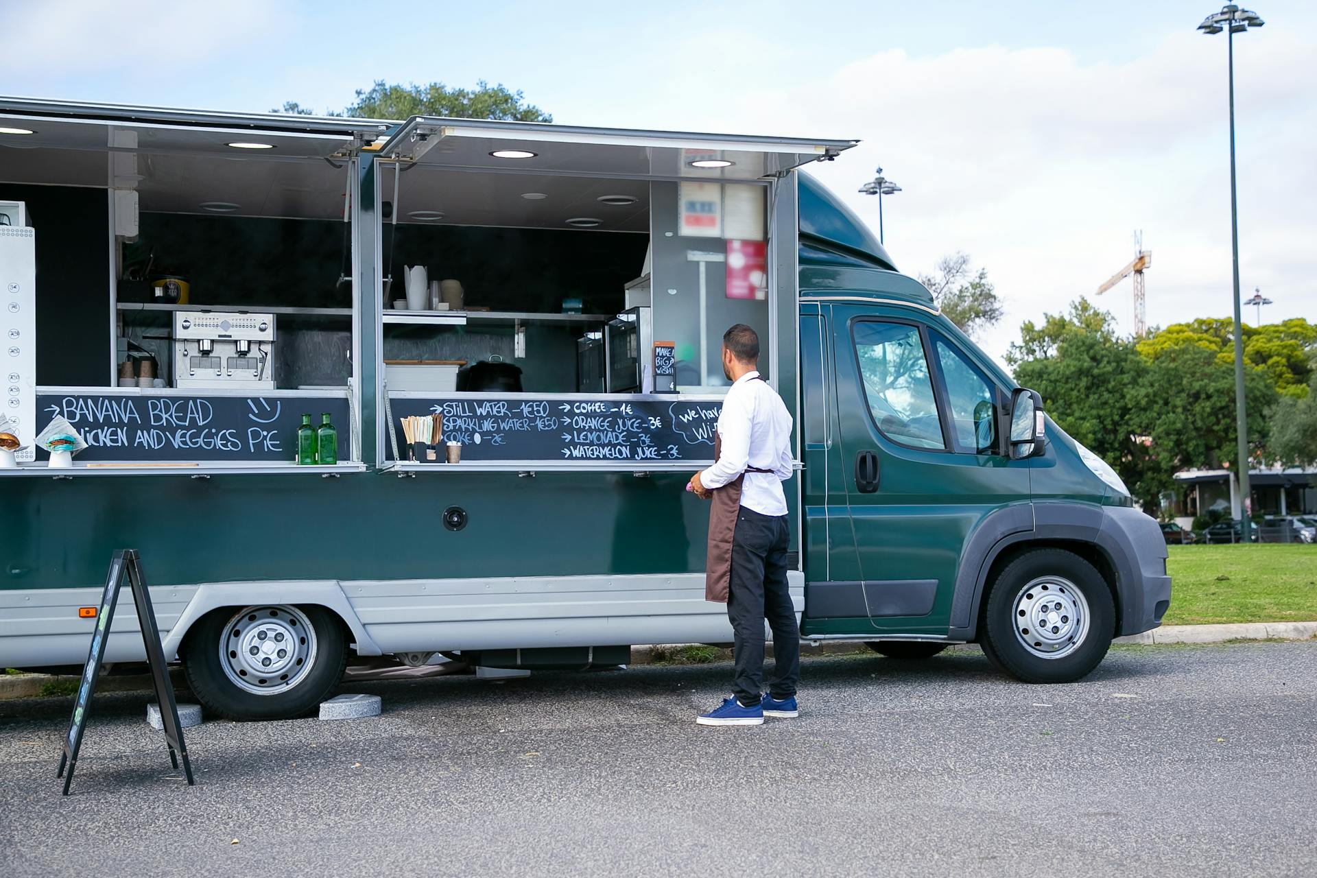 Back view full body of anonymous man in apron standing near food trailer with counter and menu on board