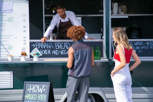 Free Ethnic salesman in uniform giving advice for choice of diverse customers of street food truck Stock Photo