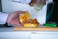 Crop anonymous male cook pouring mayonnaise sauce from bottle to fried pulled pork on bun in kitchen