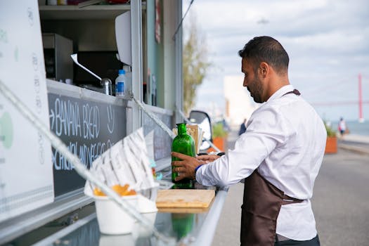 Male vendor prepares drinks at a food truck by the waterfront.