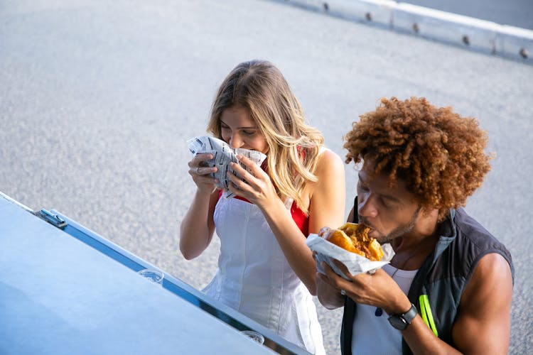 Multiethnic Couple Eating Junk Food On Street