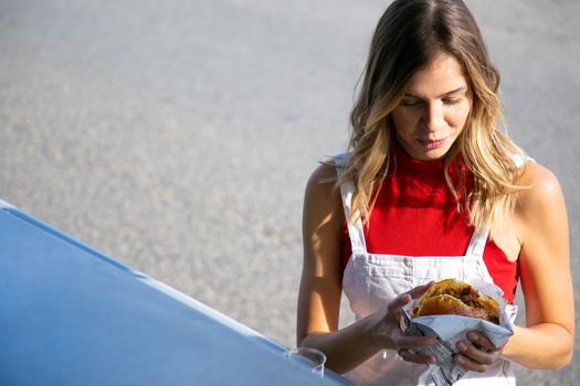High angle of serious female shopper with burger at counter of street food truck in daytime
