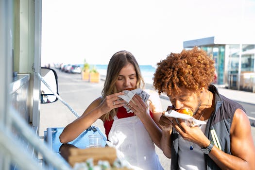 Hungry multiethnic couple eating with appetite hamburgers at food truck while spending time together