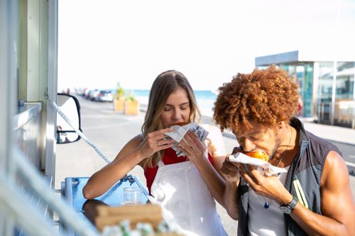 Free Hungry multiethnic couple eating with appetite hamburgers at food truck while spending time together Stock Photo