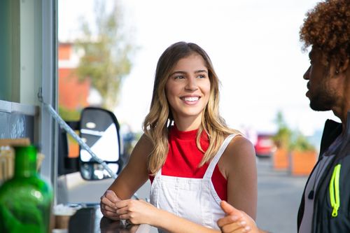 Free Smiling girlfriend talking to African American boyfriend while standing at counter of food truck Stock Photo