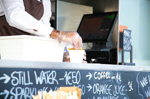 Free Low angle of crop anonymous male seller with cup of fried food at counter with cashier Stock Photo