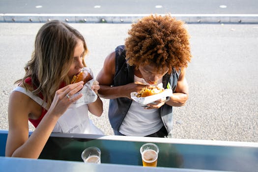Two people enjoying tasty burgers and drinks at a street food counter.