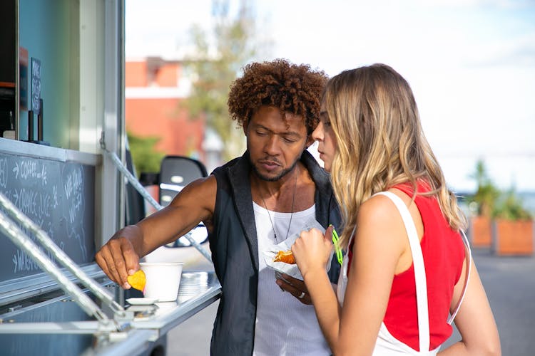 Multiethnic Young Diverse Couple Eating Fast Food In Truck Cafe