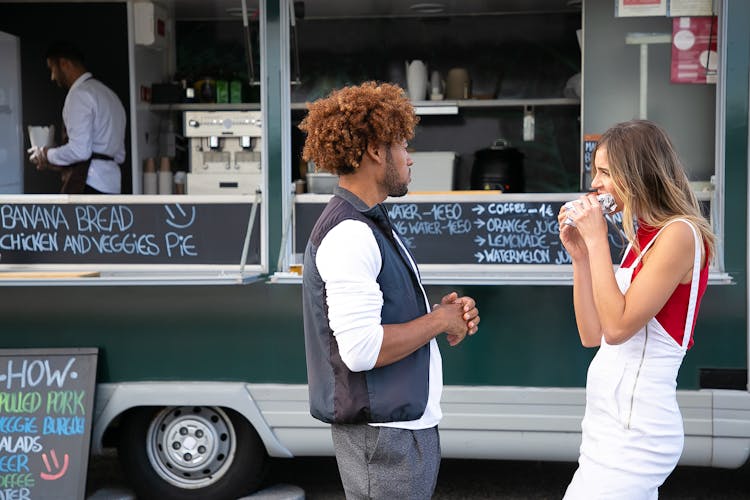 Young Diverse Couple Eating Takeaway Sandwich While Standing Near Food Truck