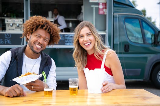 Smiling friends enjoying a meal and drinks at an outdoor food truck, sharing joy and leisure time.