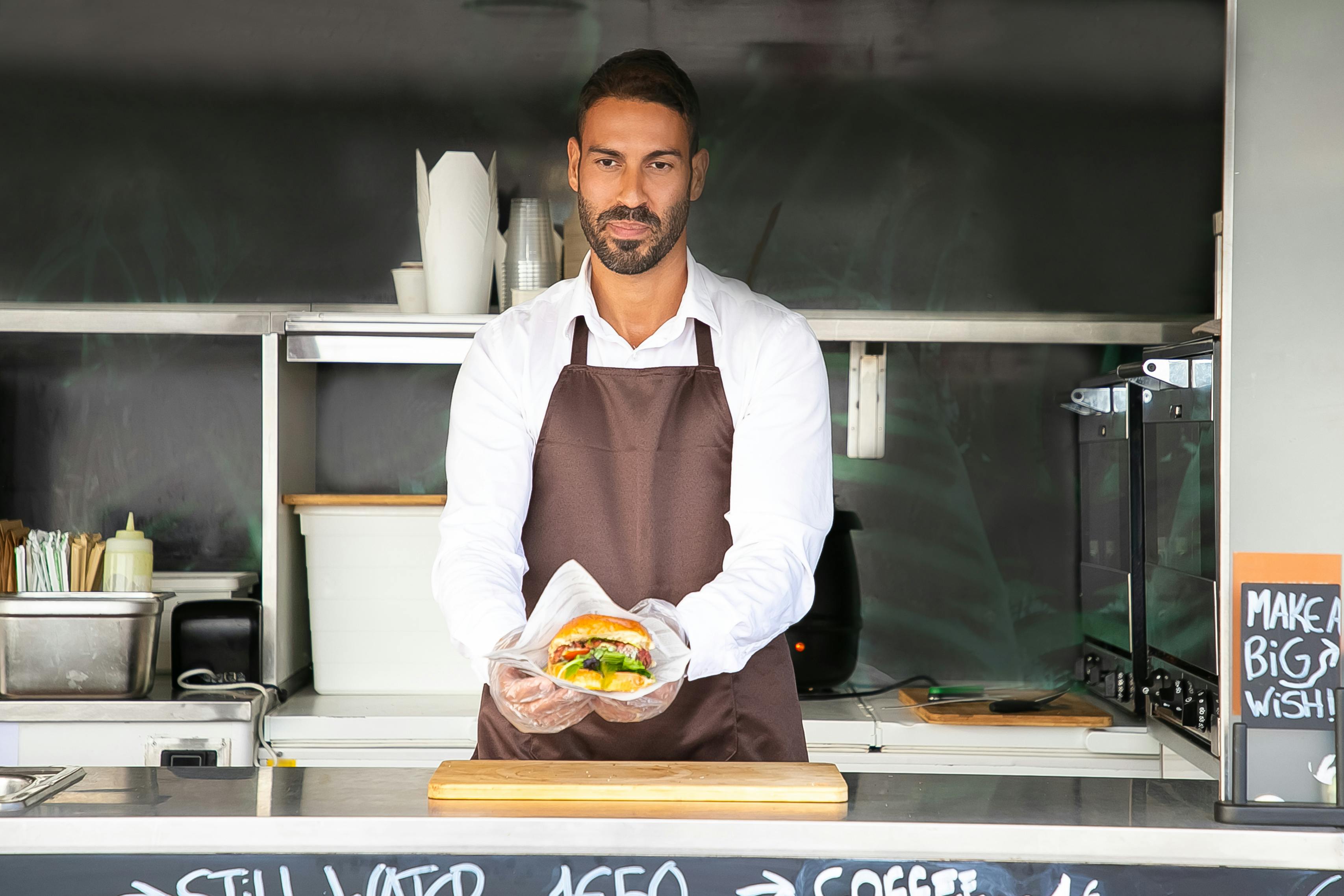 Young ethnic chef showing tasty burger in road cafe · Free Stock Photo