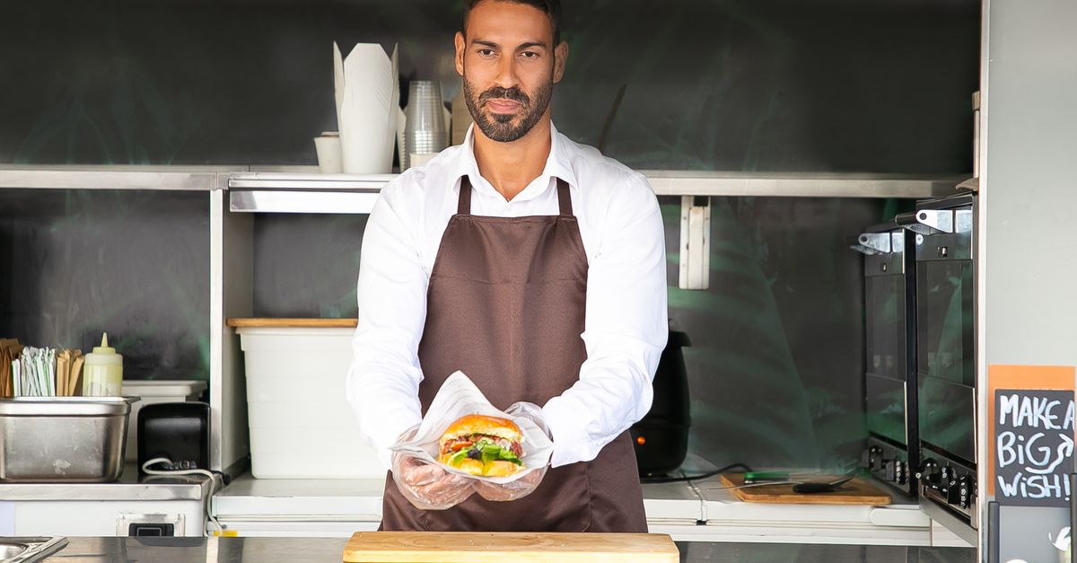Young ethnic chef showing tasty burger in road cafe · Free Stock Photo