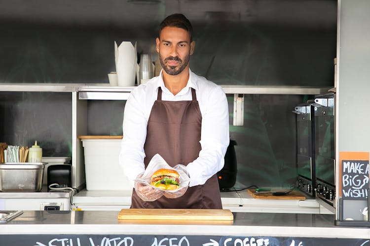 Young Ethnic Chef Showing Tasty Burger In Road Cafe