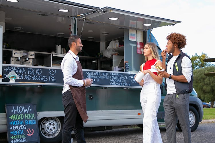 Young Multiracial Couple Eating Takeaway Fast Food And Walking Near Ethnic Chef Standing Near Van