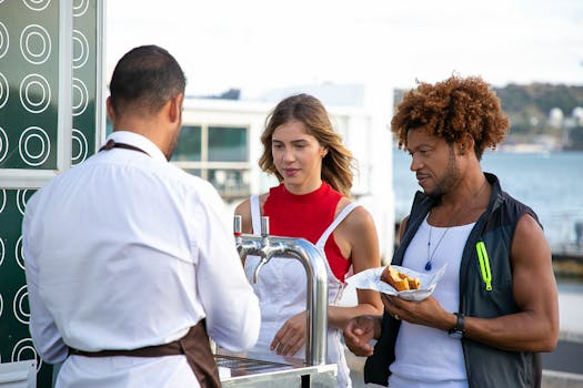 Back view of unrecognizable male bartender pouring draft beer for diverse young friends eating burger in road cafe located near lake