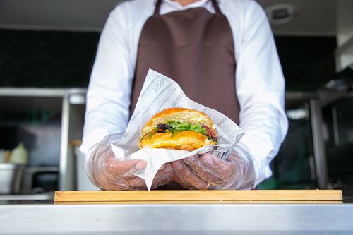 Free From below of crop anonymous cook in apron standing in food truck and giving delicious hamburger in daylight Stock Photo