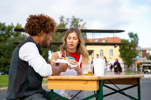 A couple sitting outside enjoying street food and drinks on a sunny day.