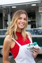 Happy woman with blond hair in casual clothes standing with blue burger against food truck on street in daytime