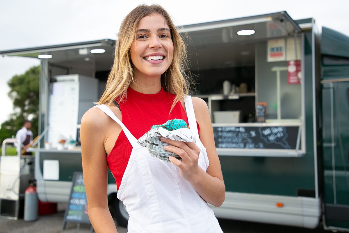 A smiling customer holding a wrapped burrito in front of the Fuego Seoul truck