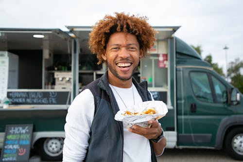 Joyful black man with sandwich standing against food truck