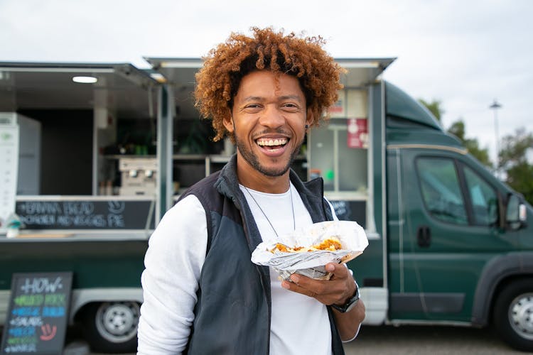 Joyful Black Man With Sandwich Standing Against Food Truck