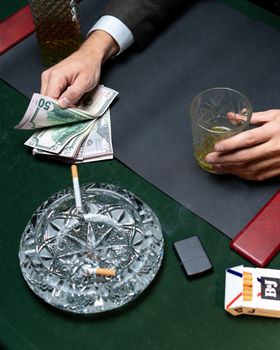 特写镜头中，精致的餐桌上摆放着威士忌、现金和点燃的香烟