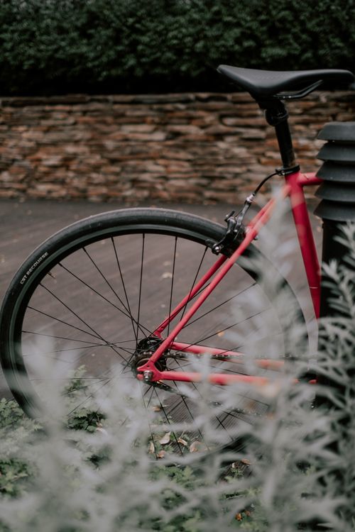 Free Close-up of a red bicycle wheel near a stone wall with plants, creating an urban setting. Stock Photo