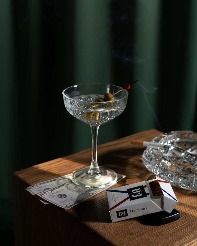 A Cocktail Drink And Cigarettes On A Wooden Table