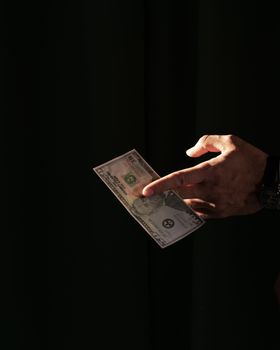 黑色背景下，手持美元纸币的手部特写突出了金融主题
