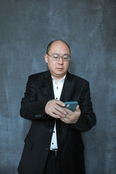 Professional bald man in a black suit using a smartphone, focused and engaged.