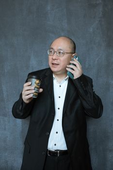 自信的商人拿着咖啡，在带纹理的墙壁背景下打电话