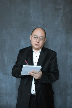在专业环境中，一位穿着西装的亚洲人正在笔记本上书写