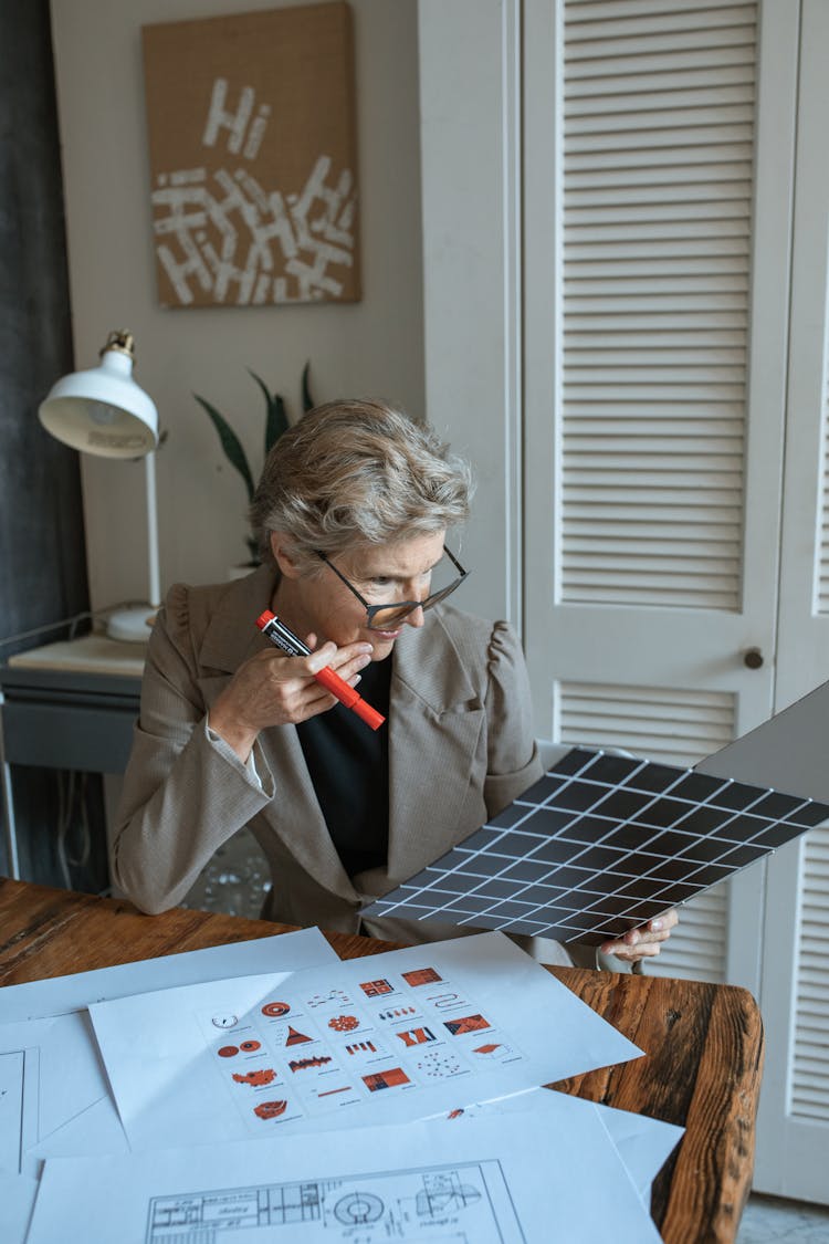 An Elderly Woman Reading A Document On A Binder While Holding A Red Marker