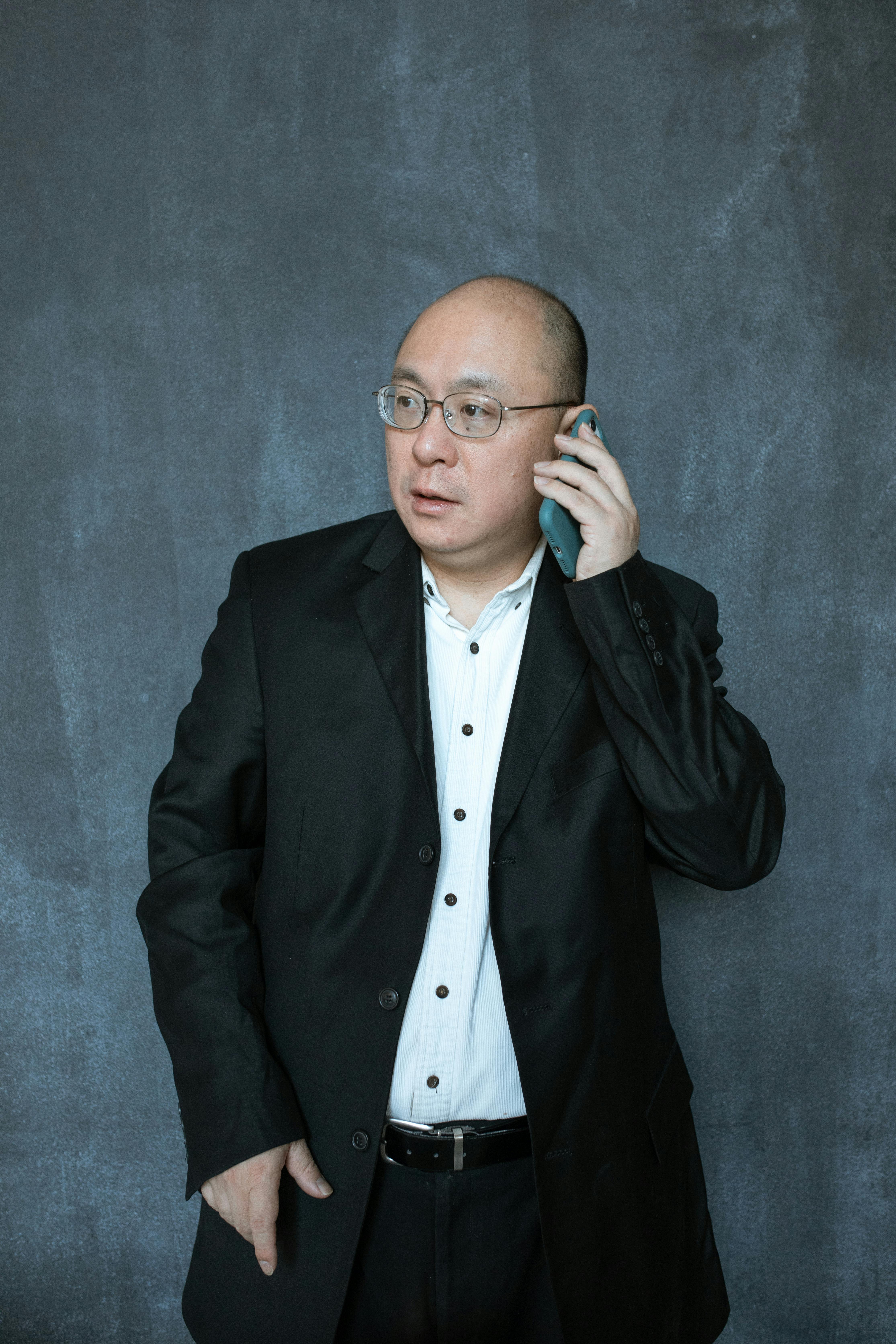 Asian man in a black suit using a smartphone in a studio setting.