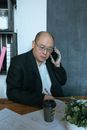 一位身穿黑色西装的成年男子在办公桌前一边打电话一边做笔记
