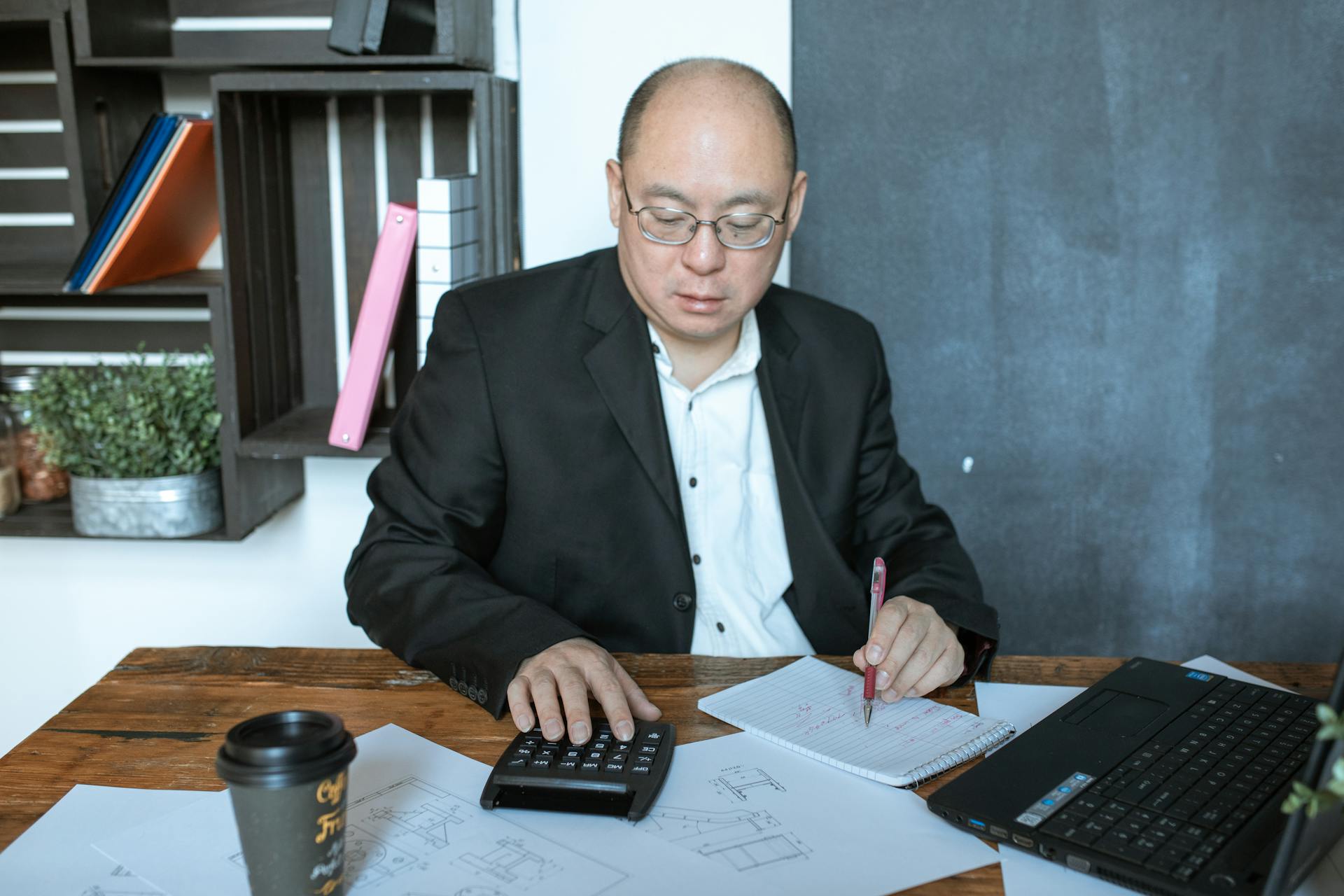 Asian businessman working with calculator and notes at his desk in a modern office space.