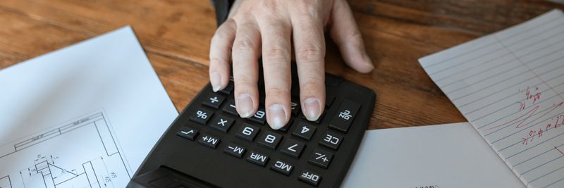 Hand using calculator for architectural calculations on blueprints.