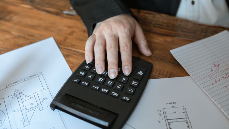 Hand using calculator for architectural calculations on blueprints.