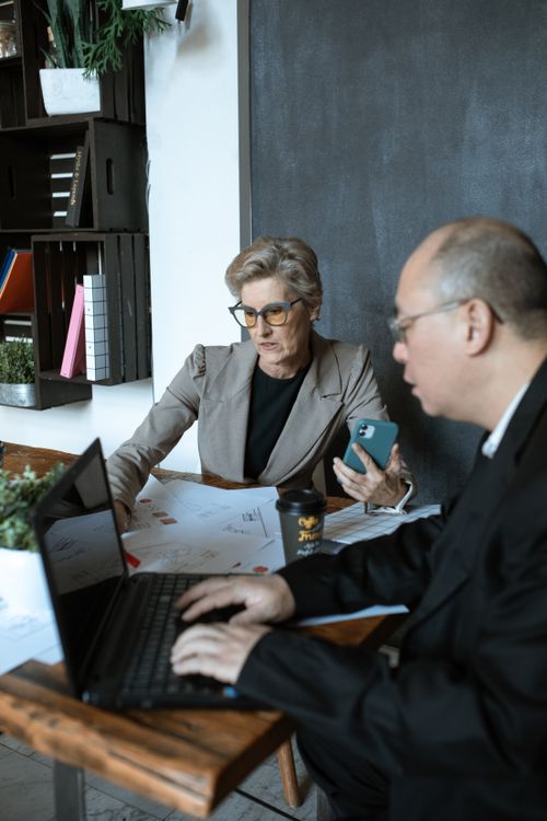 Free Two senior colleagues discussing a project in a modern office setting, using laptops and mobile devices. Stock Photo