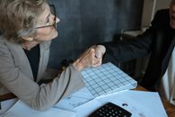 在办公室环境中，一位穿着西装的高级女性隔着桌子握手
