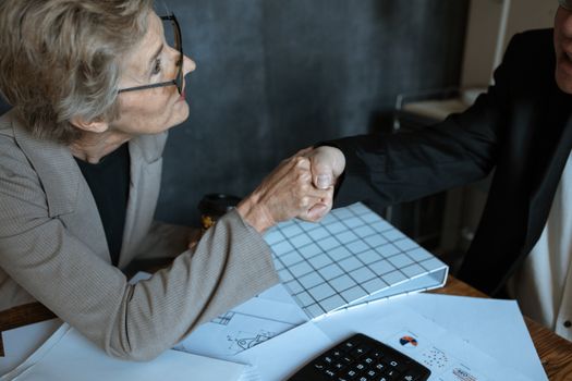 在办公室环境中，一位穿着西装的高级女性隔着桌子握手