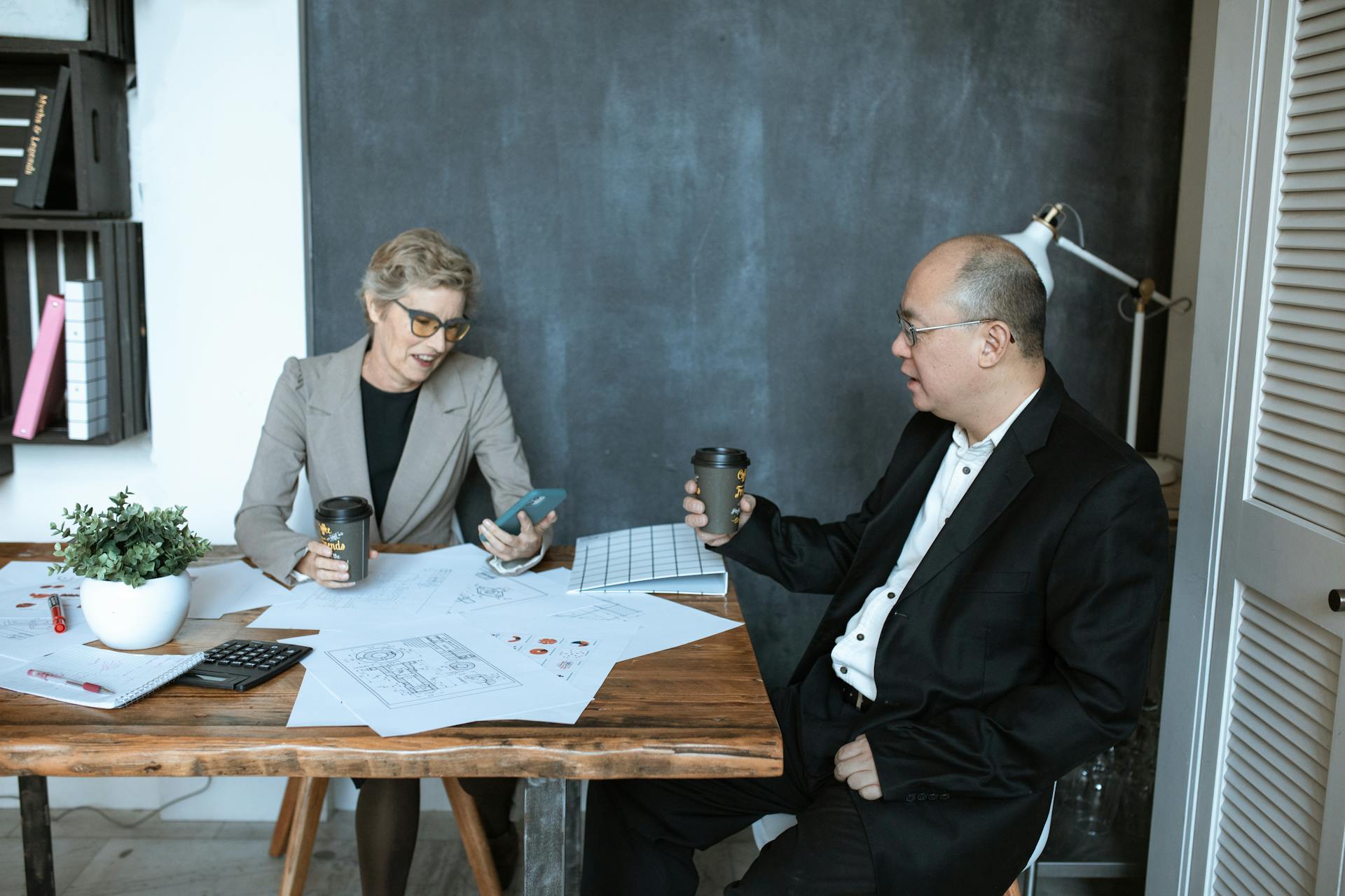 Professional meeting with two adults discussing plans over coffee in an office setting.