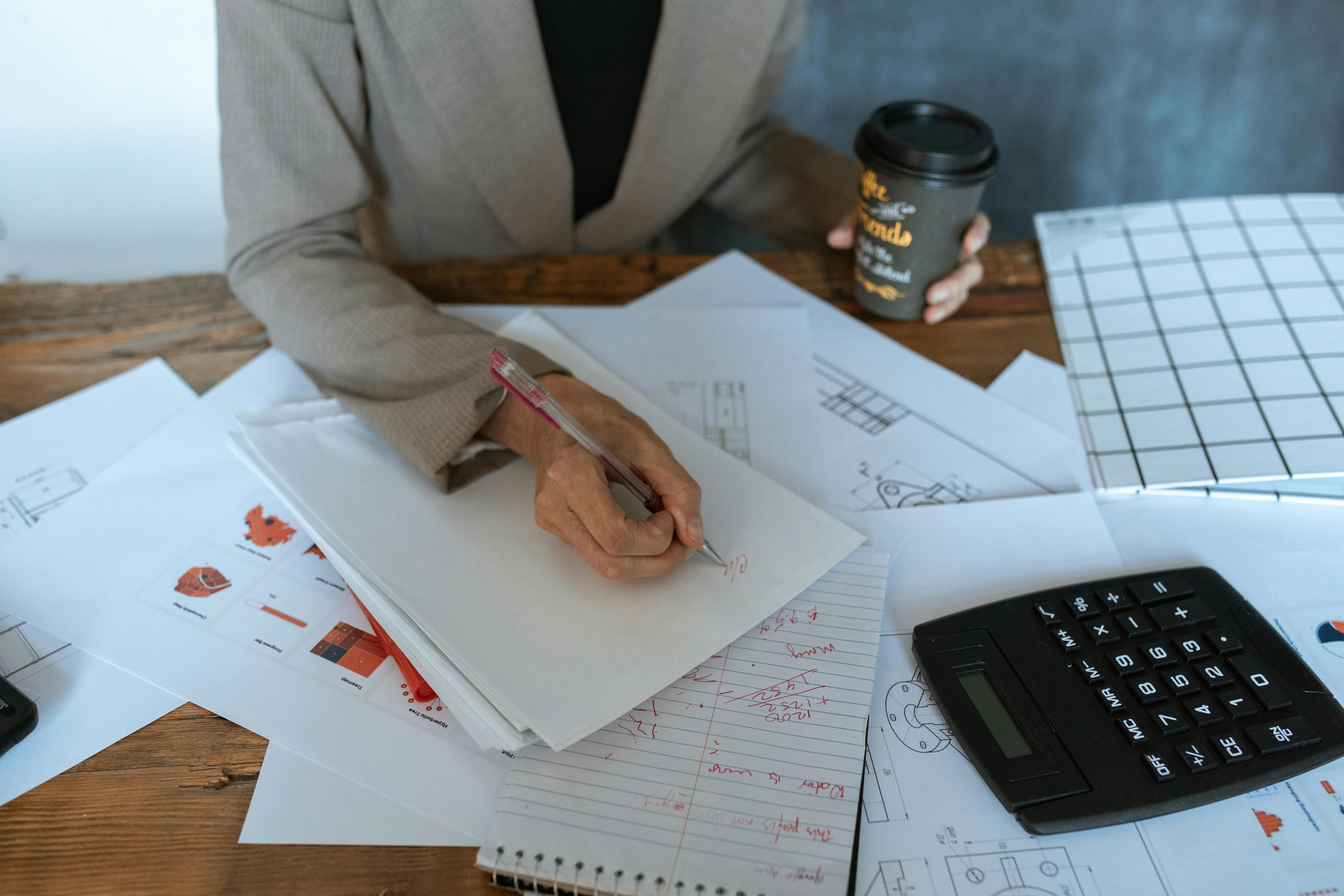 a person writing while holding a cup of coffee