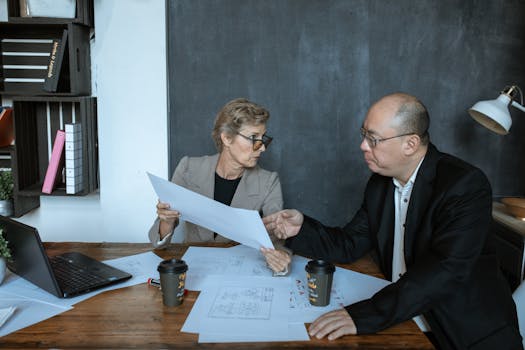 An Asian man and Caucasian woman collaborating over documents in an office setting.
