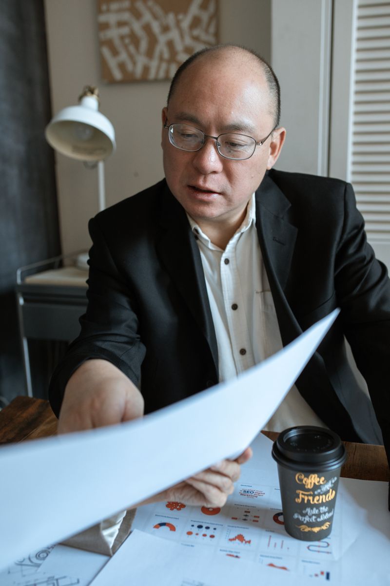 An Asian businessman analyzing documents with coffee in a modern office setting.