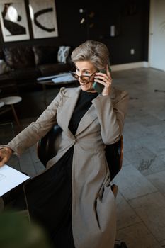 一位优雅的高级女性在现代办公室里穿着灰色外套使用手机