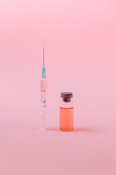 在粉红色背景的工作室里拍摄的注射器和疫苗小瓶